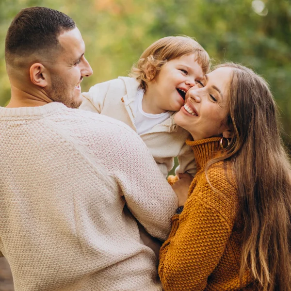 Une famille de trois personnes rit et sourit ensemble dans un décor automnal coloré.