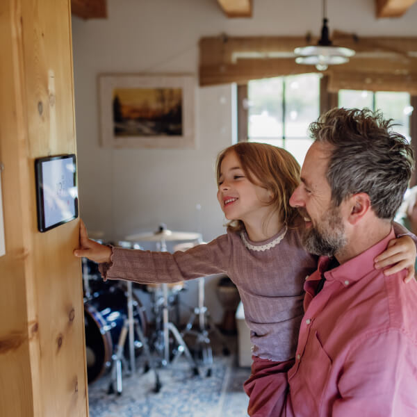 Un père et sa fille regardent un écran, s'intéressant à la domotique résidentielle pour une maison intelligente au Québec. 