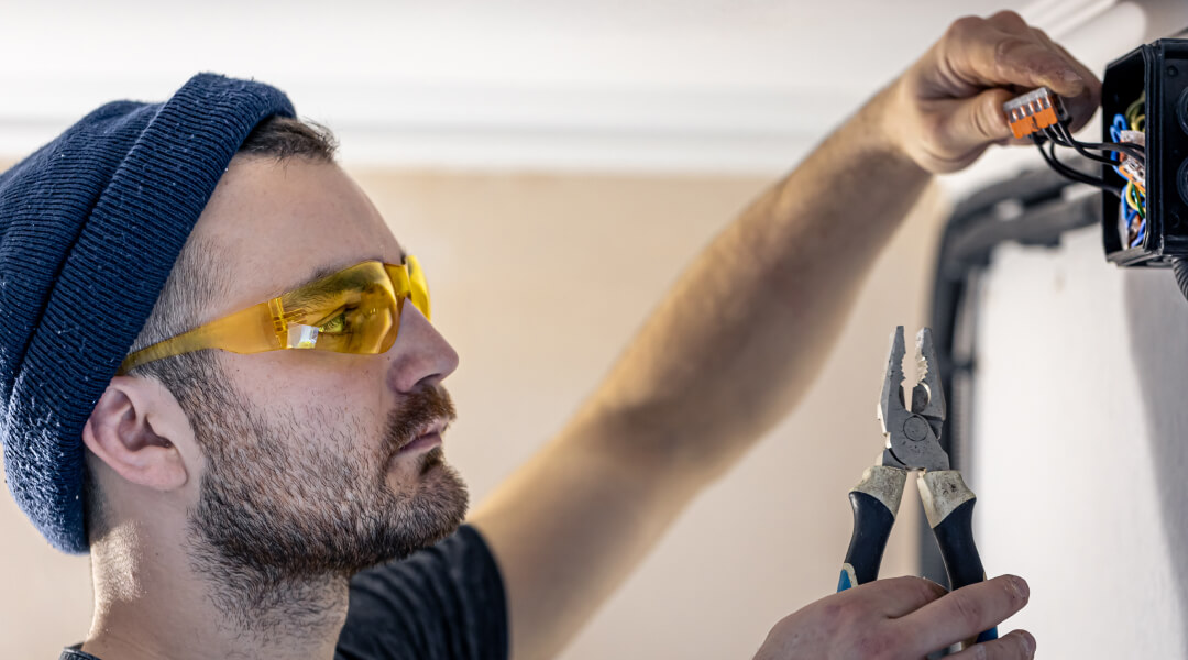 Un homme en chapeau et lunettes installe un interrupteur électrique avec soin