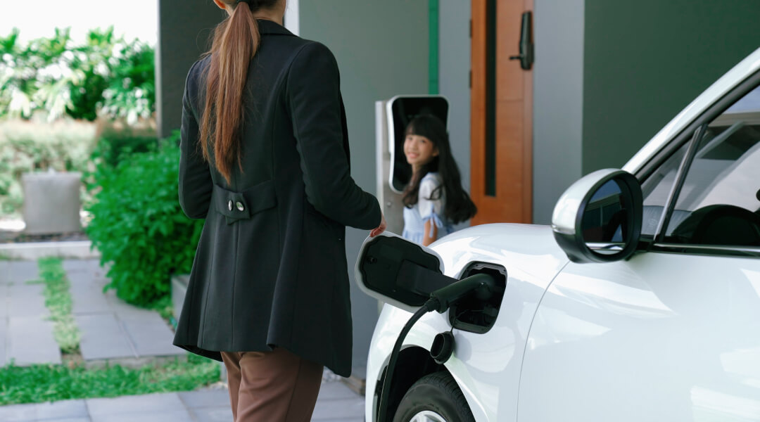 Une femme recharge sa voiture électrique dans son garage, réfléchissant à l'emplacement idéal pour la borne de recharge.