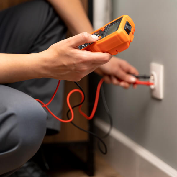 Un homme en gilet orange et lunettes de sécurité tient un multimètre lors d'une inspection électrique à Laval.