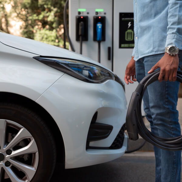 Un homme recharge sa voiture électrique à une station de recharge, soulignant l'importance des subventions pour l'électromobilité.